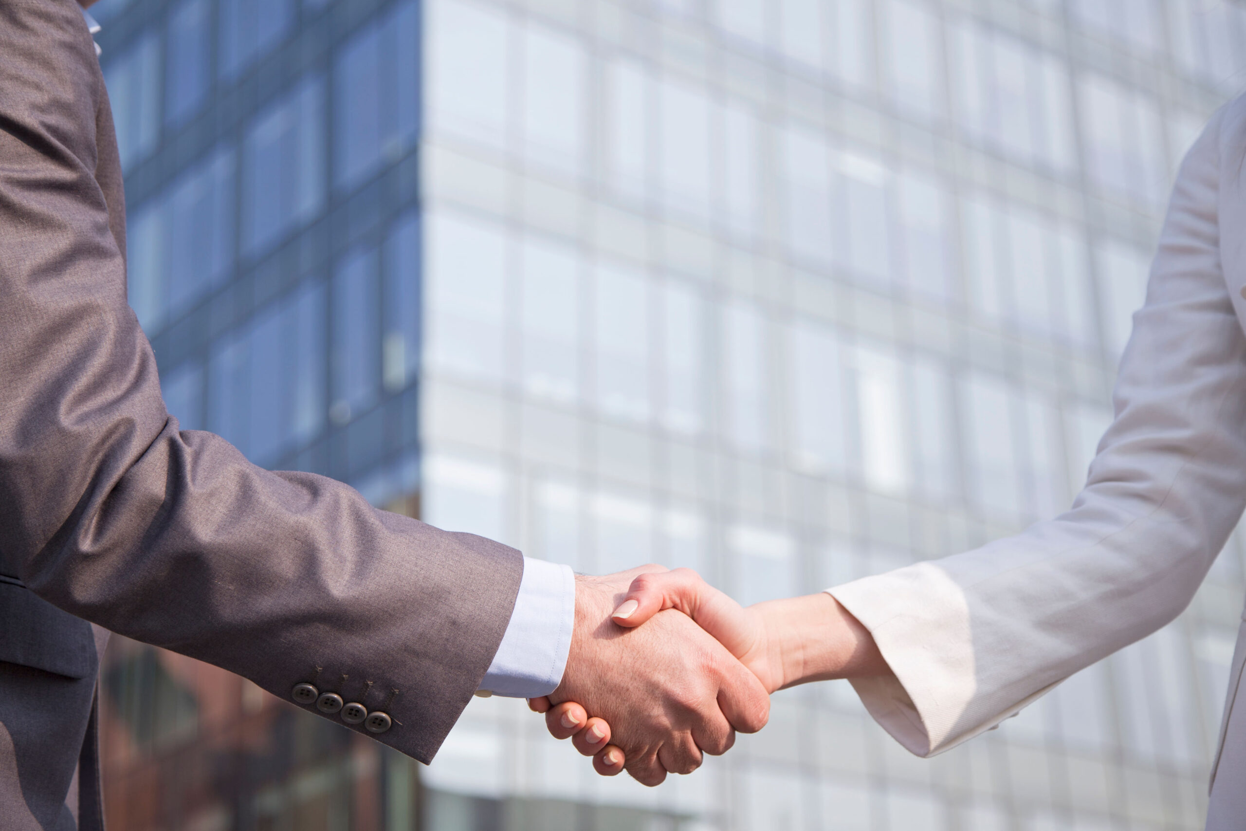 Two partners shaking hands and smiling outdoors